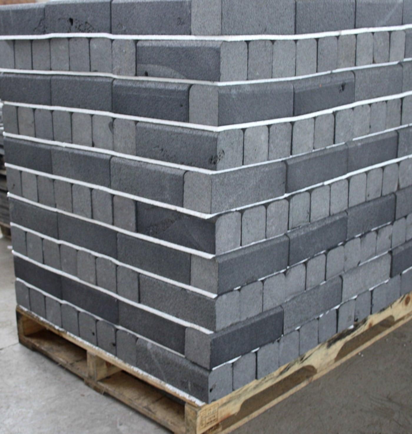 Basalt-Pflastersteine gestapelt und umreift auf einer Palette im Hof